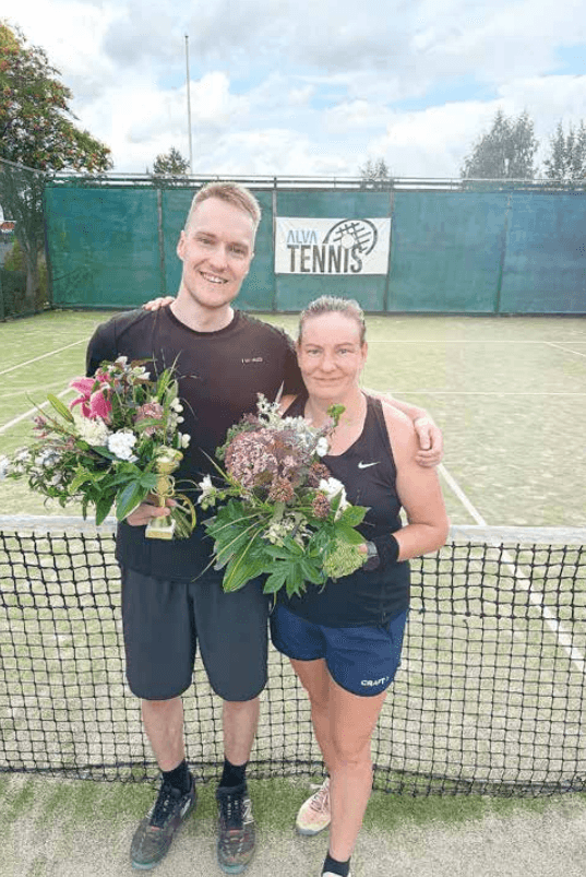 Ville Perkkola & Eija Tolmunen hymyilevät kukkakimput kädessään tenniskentällä.