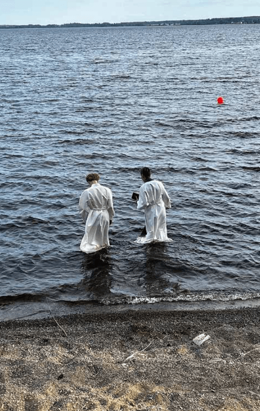 Pari nuorta kahlaavat rantavedessä valkoinen alba päällään. He valmistautuvat kasteeseen.